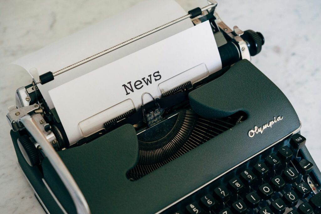 An old typewriter is posed at an angle, with a piece of white paper and the word News on it.